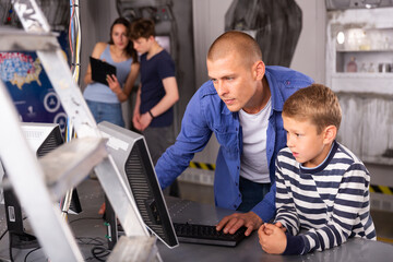 Interested young man with his tween son using computer to find solution to puzzle in escape room stylized as abandoned bunker
