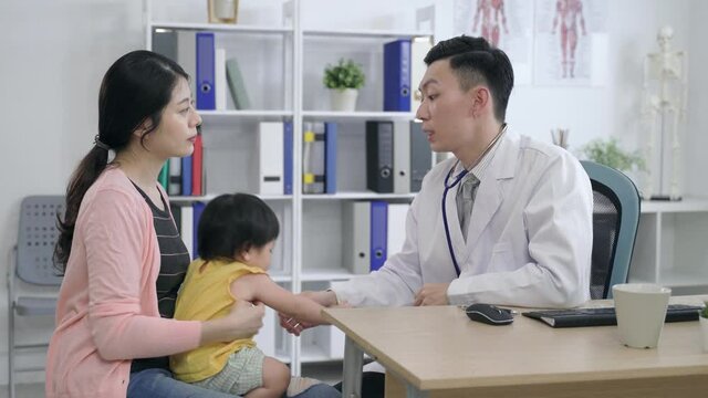 asian specialist is removing the stethoscope after examine and talking to the mother while gently pushing the girl back to prevent falling at clinic.