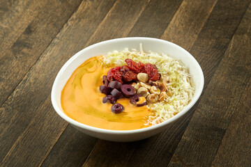 Appetizing cream soup with various cheeses, hazelnuts, olives and sun-dried tomatoes in a white plate on a wooden background