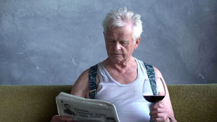Elderly man drink wine and read newspaper at home 