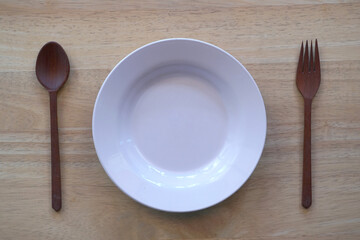 Empty plate with spoon and fork on wood background.