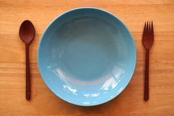 Empty blue plate with spoon and fork on wood background.