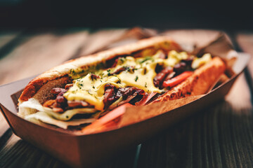 Philly cheese steak sandwich with meat, vegetables, cheese and sause in box on wooden table. street...