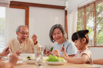 Asian extended family having breakfast together at home. Asian Big family grandparents parents and kid enjoy eating and talking with happy moment.