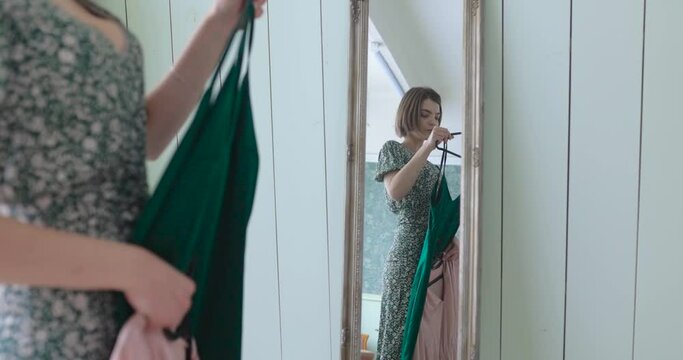 beautiful young woman trying on dress getting dressed looking in mirror choosing outfit fashion choice putting on clothes enjoying positive self image feeling confident at home 4k footage
