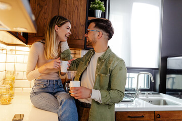 Young couple enjoying in cozy kitchen, drinking a coffee and talking something funny.