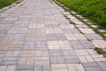 Concrete bricks footpath on the green grass in the park, abstract background of tiles, footpath, sidewalk,