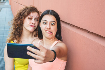 two girls of generation z take pictures with their mobile phone and make grimaces, two sisters make...