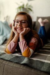 Obraz premium Close up photo of cute smiling little girl, laying on stomach at couch, chilling and relaxing.