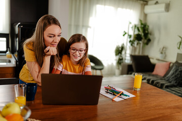 Beautiful smiling mom and cute daughter is using laptop and searching for cartoons.