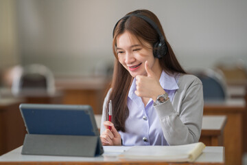 Young interactive happy Asian teenage girl university student studying and presenting her lesson online via video call on a digital tablet in the classroom alone herself. Education stock photo