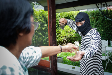 male thief wearing black mask Carrying large knives into the house of an elderly woman to rob and...