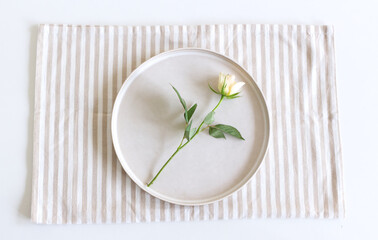 Festive table setting. Empty plate, napkin and white rose on white table. Top view, flat lay, copy space.