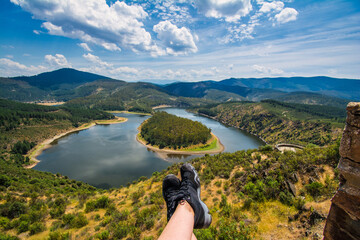 Fototapeta na wymiar Hiker Feet Resting And Contemplating Beautiful Views Of Nature. Meander Of The River Alagón Known As Meander Of Melero. Located In Extremadura, Spain. Nomadic life concept.