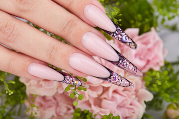 Hand with long artificial purple french manicured nails decorated with rhinestones and pink rose...