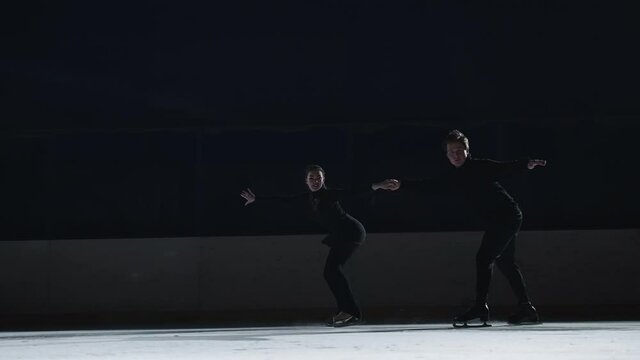 Pair figure skating on the rink. A man and a woman in a counter-light perform elements of the Olympic program together in slow motion