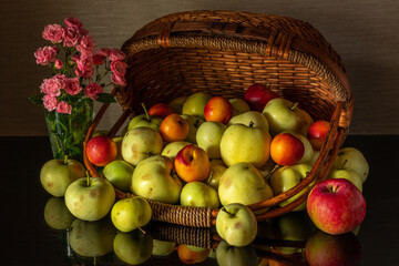 Basket of fruits. Autumn still life with apples and other fruits on a dark background. Light from the window.