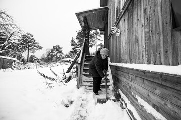 Old woman cleans the snow near rural home. Black and white photo.