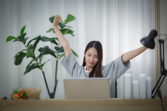 Asian Woman Sitting At Home Working In Front Of A Laptop Arms Spread Out In Exhaustion