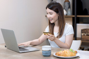 Happy Asian woman shopping online with laptop computer and paying with credit card.