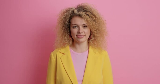 Pretty young woman with curly hair smiles pleasantly listens pleasant news dressed on formal clothes has talk isolated over pink background. Fashionable businesswoman expresses positive emotions
