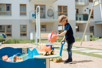 3 year old child plays in open playground in yard with toys. Children's leisure concept