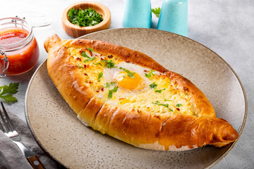  A traditional dish of Georgian cuisine, Adjarian khachapuri with cheese and egg and spicy tomato sauce adjika on the plate