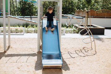Child 3 years old, sitting happily down metal slide in yard. Outdoor entertainment concept for kids