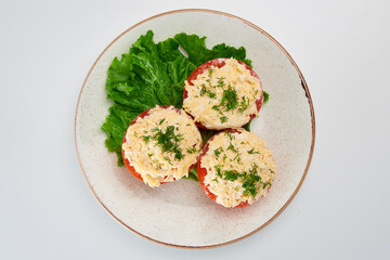 Three halves of fresh tomato with grated cheese, garlic, white sauce, sprinkled with finely chopped fresh dill, with green lettuce leaves in a white round plate on a white background.