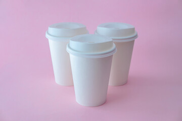 Three white paper coffee cups on pink background, coffee cup mock up.