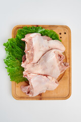 Three fresh chicken backs with green lettuce leaves and black pepper peas on a rectangular wooden chopping board on a white background.