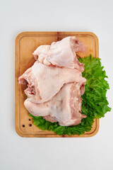 Three fresh chicken backs with green lettuce leaves and black pepper peas on a rectangular wooden chopping board on a white background.