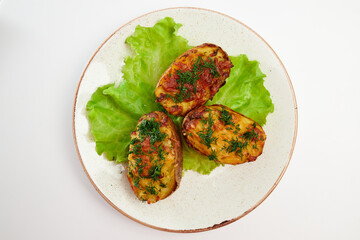 Baked three potato halves with skin, sprinkled with finely chopped dill with three green lettuce leaves in a round white plate on a white background.