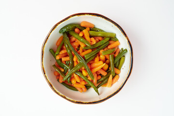Garnish of boiled green beans, young carrots in a round white plate on a white background.