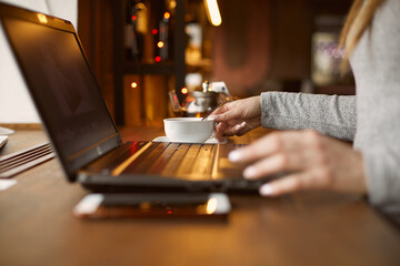 Girl ordering tea in a cafe. Works for a laptop. The mobile phone is on the table. Remote work and freelance work concept.