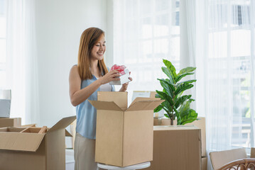 Beautiful Asian woman stands and opens a gift box from cardboard while she moved to a new house in the living room.