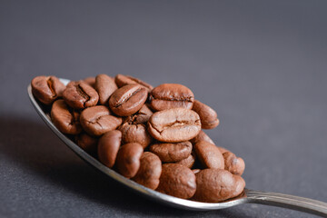 Close up to Roasted coffee beans served in silver vintage stainless steel spoon on dark background. High quality organic aroma seeds. Copy space text image
