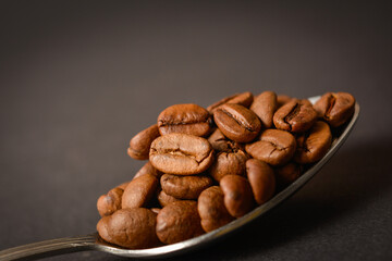 Close-up to Roasted coffee beans served in silver vintage stainless steel spoon on dark background. High quality organic aroma seeds. Copy space text image
