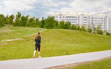 Women running, cardio workout. Young woman in sportswear runs near the park, female runner workout....