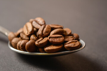 Macro shot of Roasted coffee beans served in silver vintage stainless steel spoon on dark background. High quality organic aroma seeds. Copy space text image
