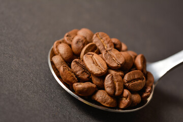 Close-up to Roasted coffee beans served in silver vintage stainless steel spoon on dark background. High quality organic aroma seeds. Copy space text image
