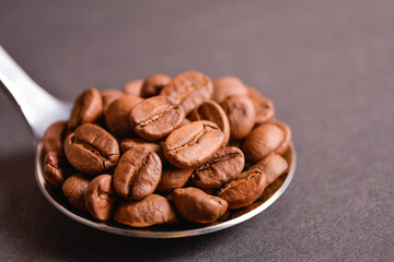 Side view of Roasted coffee beans served in silver vintage stainless steel spoon on dark background. High quality organic aroma seeds. Copy space text image
