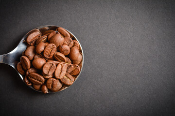 Top view of Roasted coffee beans served in silver vintage stainless steel spoon on dark background. High quality organic aroma seeds. Copy space text image
