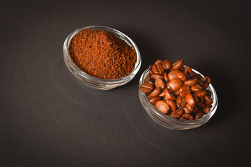 Top view of two bowls with coffee. Roasted coffee beans served in glass bowl with Ground (grinded) coffee on dark background. High quality organic aroma seeds. Copy space text image
