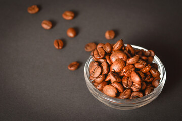 Side view of Roasted coffee beans in bowl with scattered seeds on dark background. High quality organic aroma seeds. Copy space text image
