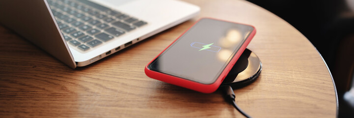 Wireless charger concept, smartphone with charging pad in modern office..