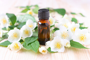 Obraz na płótnie Canvas Jasmine essential oil in a glass brown bottle on a wooden background with flowers. Complementary treatments, aromatherapy and spa, relaxation.