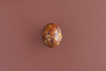 One egg, painted in brown colors, on brown background. Minimalism concept. Unusual pattern on surface of egg in form of blurred spots, handmade. Top view. Copy space.