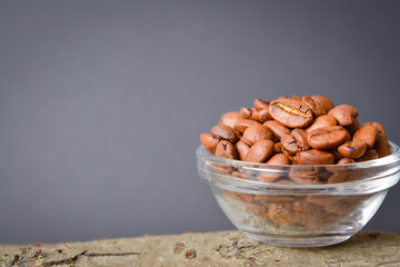 Close-up to whole coffee beans served in glass bowl on wooden log with dark background. High quality organic arabica Roasted coffee seeds. Copy space text image
