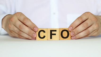 A businessman holds wooden cubes with a word CFO on a white background, with space to copy the text, business concept